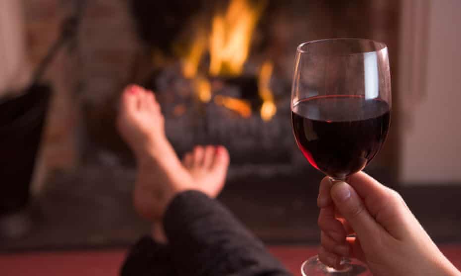 Feet warming at fireplace with hand holding wine